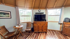 Ein gemütliches Blockhauss-Interieur mit Holzboden, einem an der Wand befestigten Fernseher, einem Holzschrank und einem Esstisch mit Stühlen.