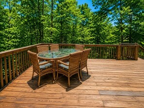 A wooden deck with a glass-top table and wicker chairs.