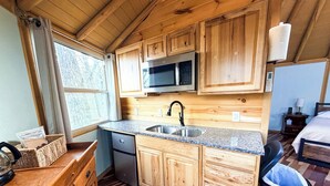 Eine kleine Küche mit Holzschränken, einer Spüle aus Edelstahl, einer Mikrowelle und einem Kühlschrank.
