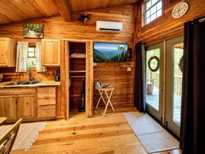 A wooden cabin interior with a kitchen, dining area, and a large window.