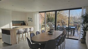Et moderne køkken med en central ø, spiseområde med et stort bord og stole, og udsigt til terrassen.