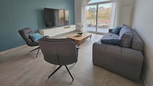 En moderne stue med en grå sofa, en grå lænestol, et træbord og et fladskærms-tv på et hvidt tv-møbel.