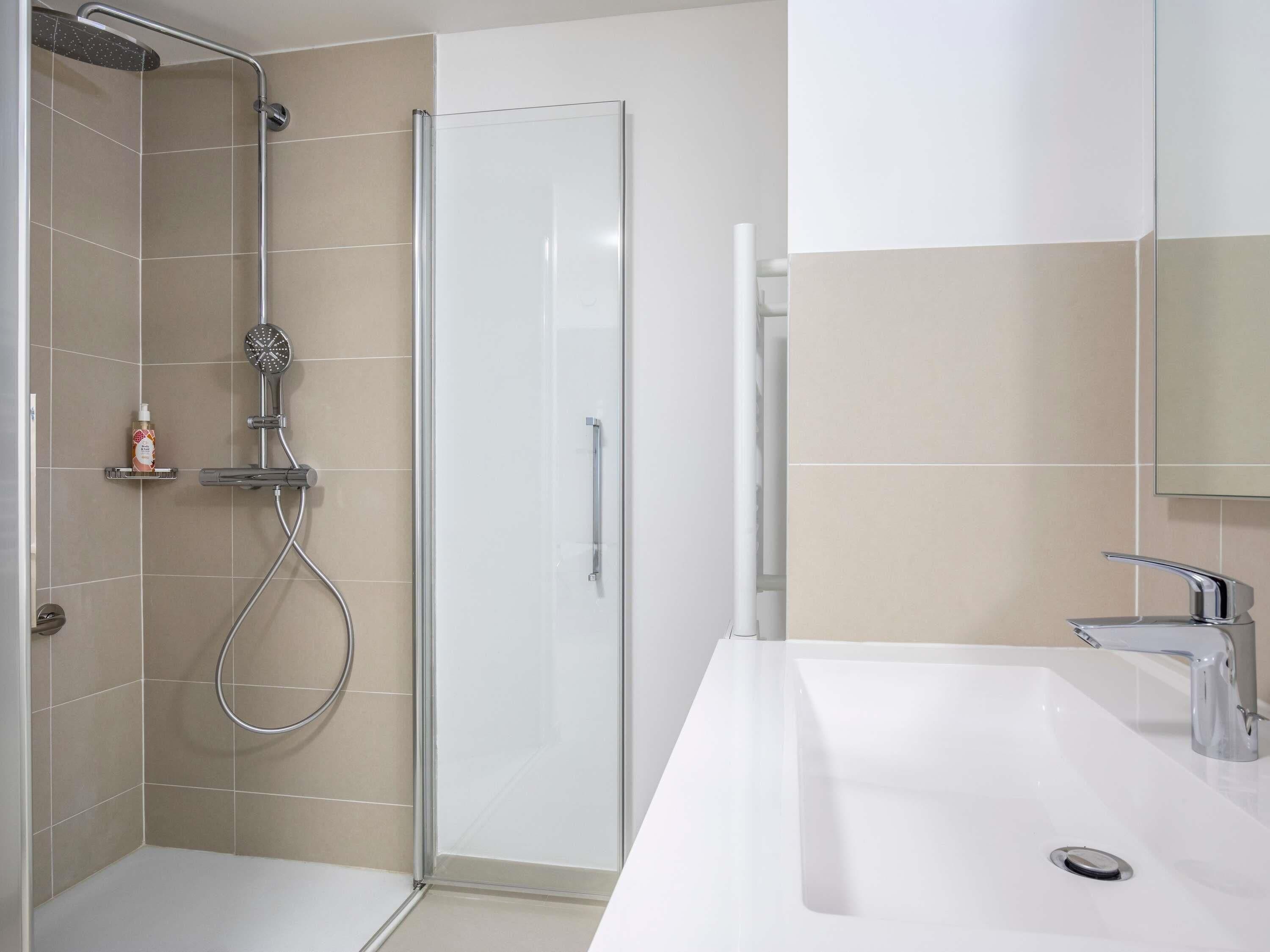 A modern bathroom with a shower, a glass-enclosed toilet, and a white sink with a mirror.