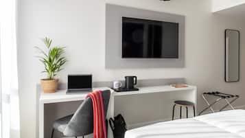 Une chambre d’hôtel moderne équipée d’un bureau, d’un ordinateur portable, d’une machine à café, d’une plante en pot et d’un lit.