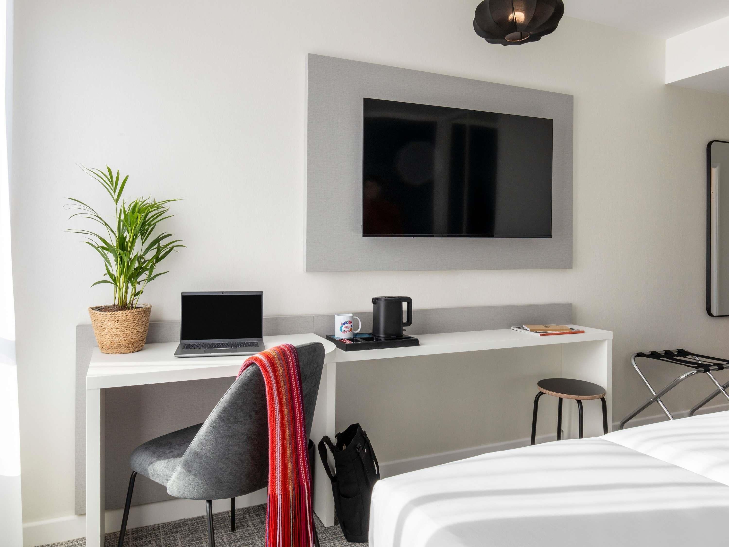 Une chambre d’hôtel moderne équipée d’un bureau, d’un ordinateur portable, d’une machine à café, d’une plante en pot et d’un lit.