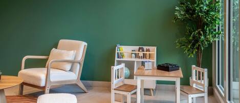 Une pièce avec un mur vert, une chaise blanche, une petite table, une bibliothèque et une plante en pot.