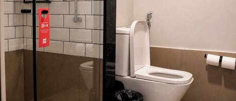 A bathroom with a toilet, a glass-enclosed shower, and a trash bin.