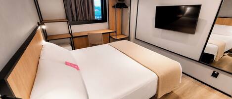 A modern hotel room with a bed, a TV mounted on the wall, a desk with a chair, and a window with curtains.
