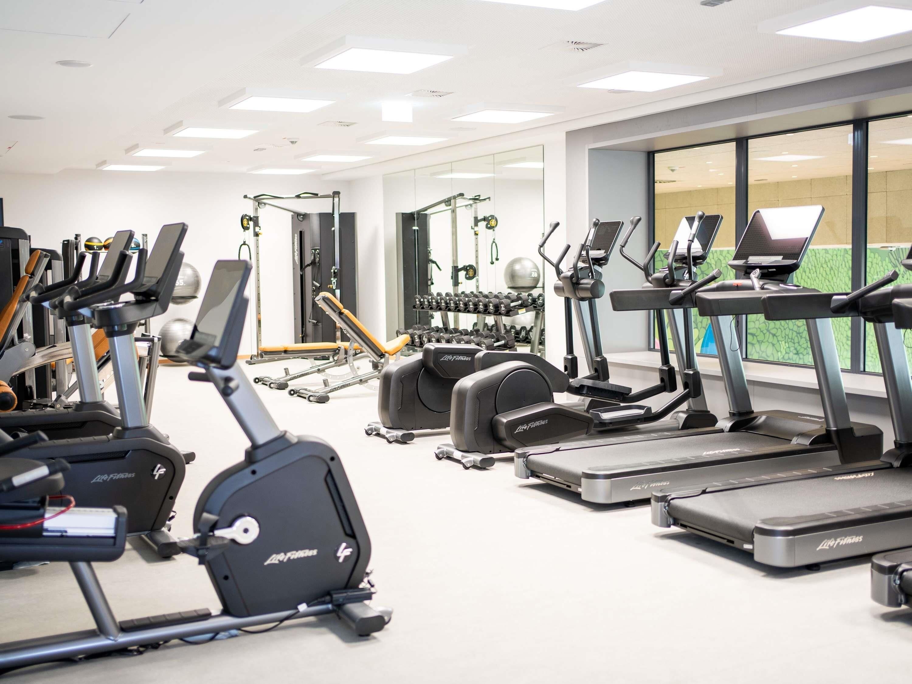 A gym with multiple cardio machines, weightlifting equipment, and a mirror wall.