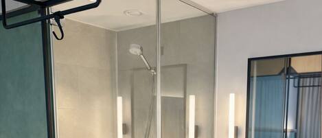 Un baño moderno con ducha envuelta en vidrio, un lavabo redondo y un espejo sobre él.