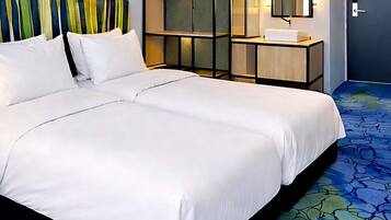 Habitación de hotel con cama doble, mesita de noche con lámpara, un espejo y una alfombra azul estampada.