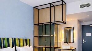 Habitación de hotel con una cama grande, cabecera de madera, mesita de noche con espejo y alfombra azul estampada.