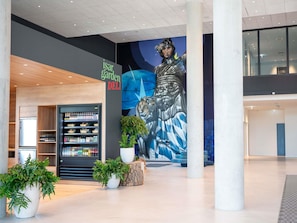 A modern interior with a deli counter, a mural, and potted plants.