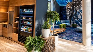 Un interior moderno con una delicatessen llamada 'Isar Garden Deli', una máquina expendedora y un mural de una figura con un león.