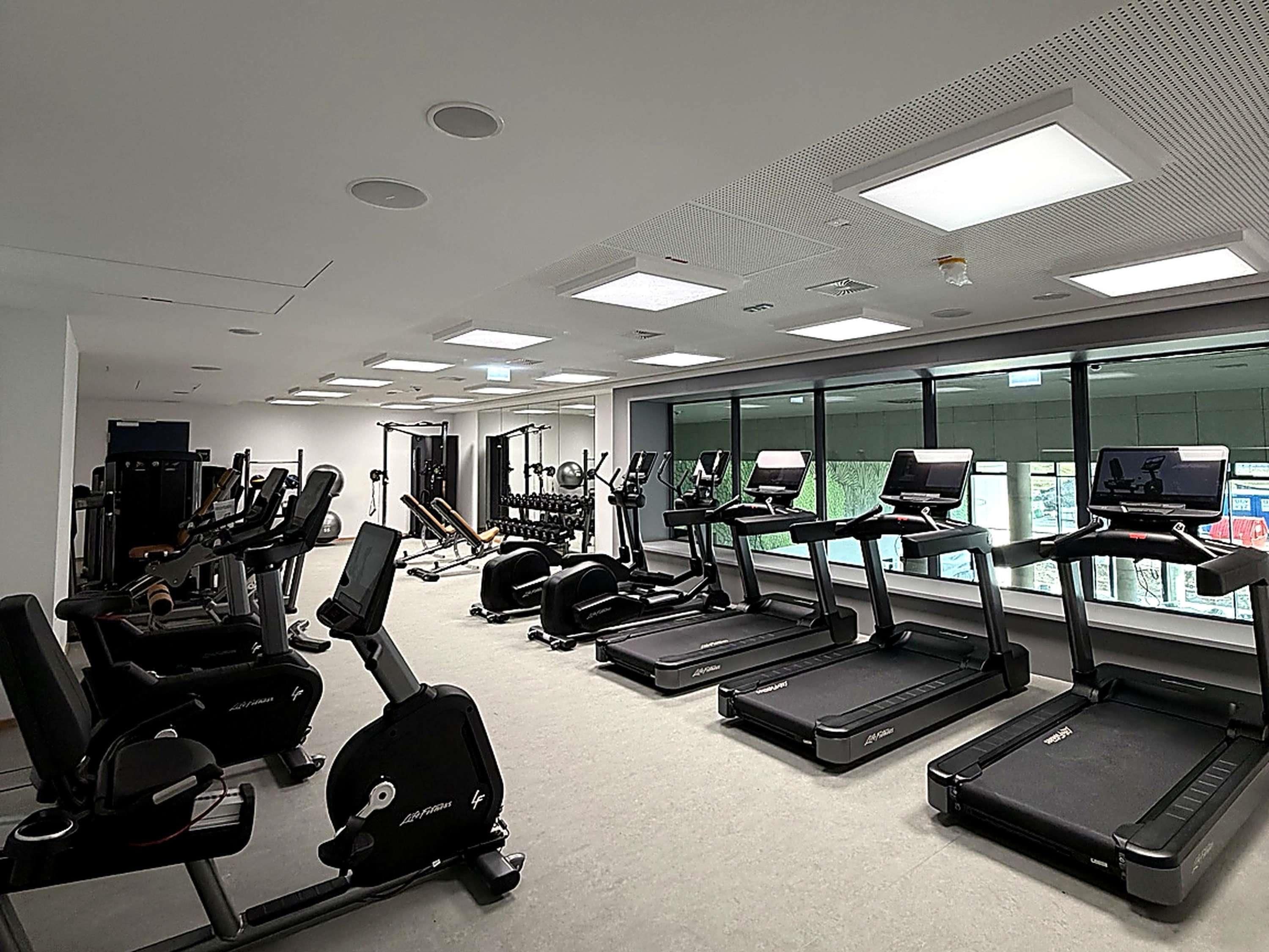 Et fitnesscenter med forskellig træningsudstyr, herunder løbebånd, crosstrainere og styrkemaskiner.