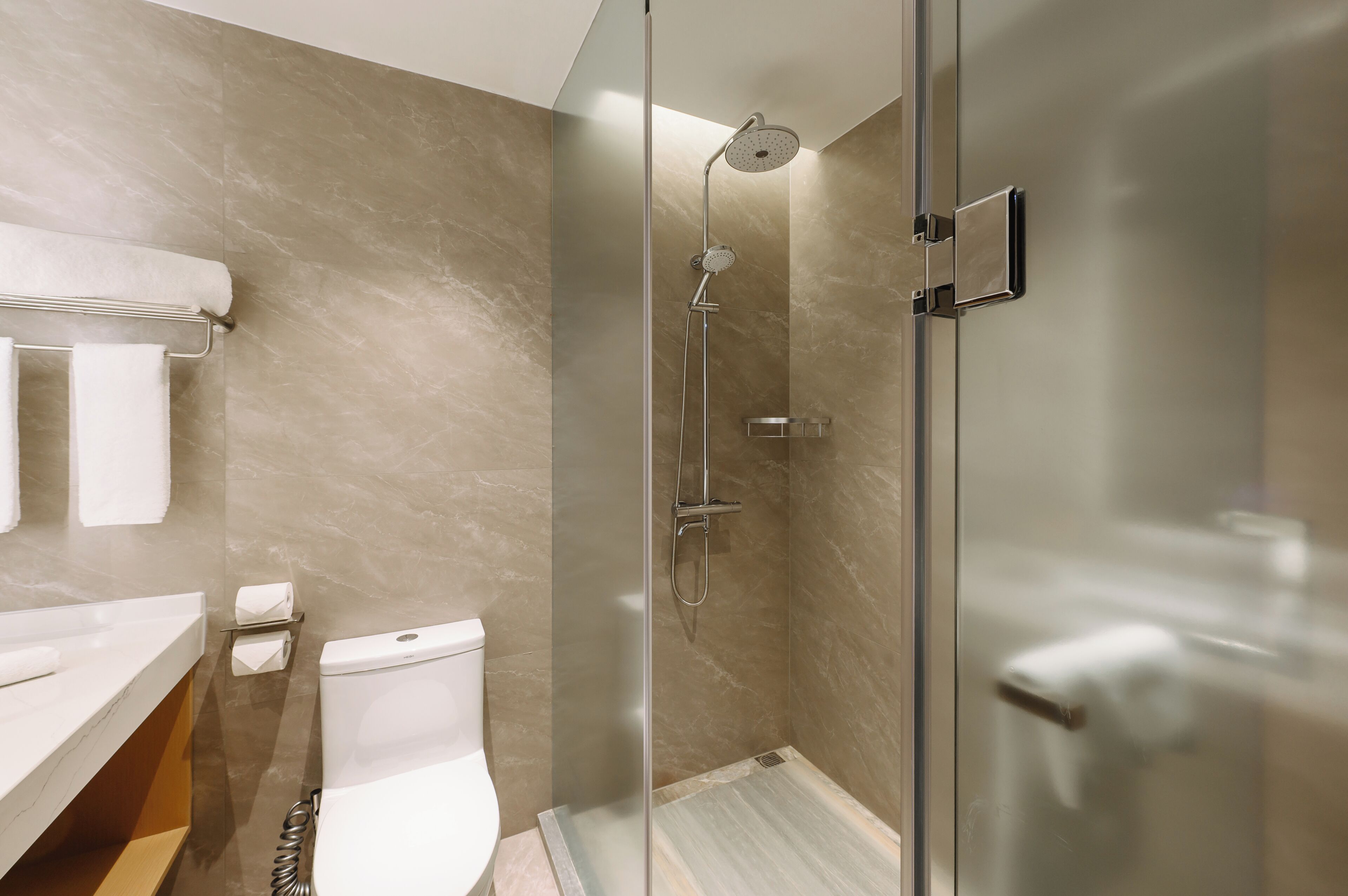 Une salle de bain moderne avec une douche à parois de verre, des toilettes et un porte-serviettes.