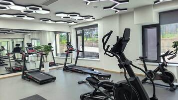 Un gimnasio con cintas de correr, bicicletas estáticas y un espejo grande.