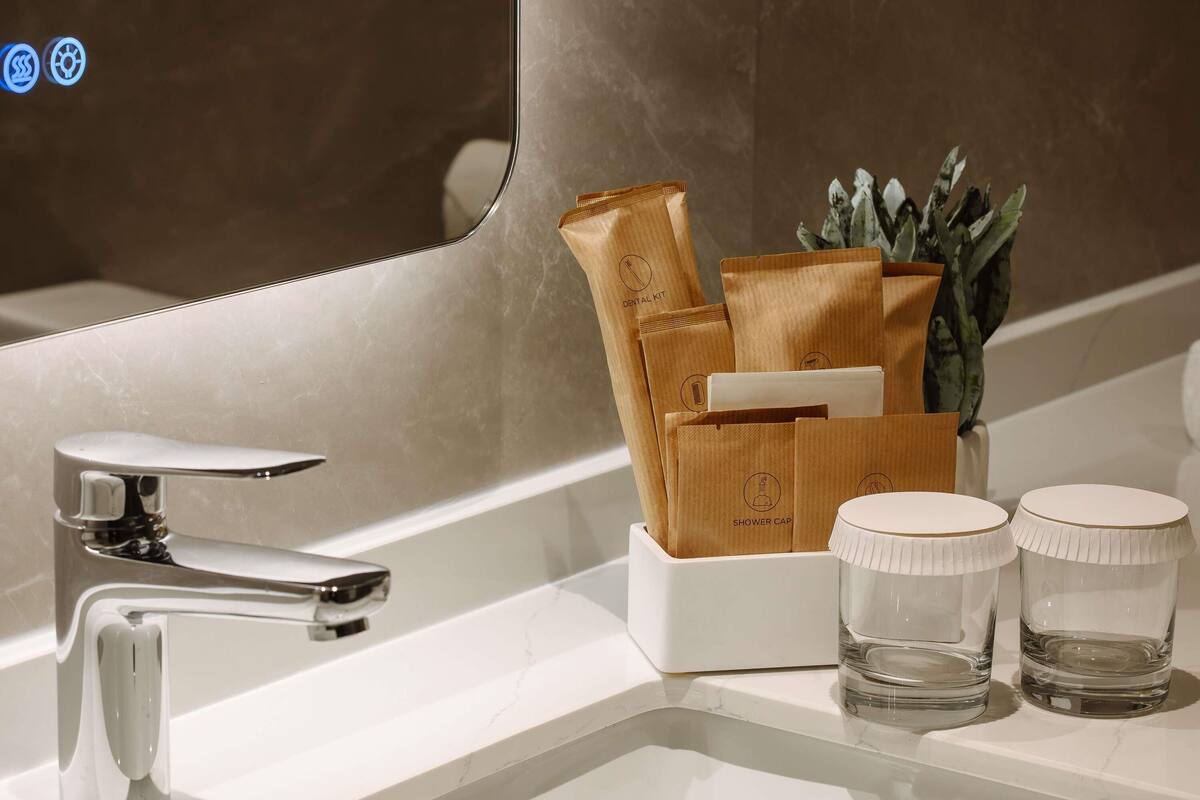 A bathroom with a modern sink, a chrome faucet, a shower cap holder, and two clear glass containers.