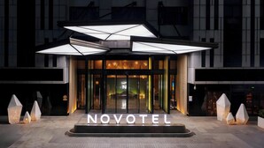 Entrada de hotel con fachada de vidrio, señalización iluminada y luminarias geométricas.