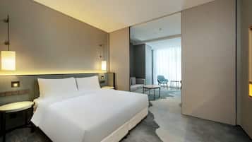 A modern hotel room with a large bed, bedside tables, a desk, and a view of the adjacent room.