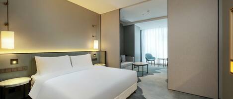 Quarto de hotel moderno com uma cama grande, mesas de cabeceira, uma escrivaninha e vista para o quarto vizinho.