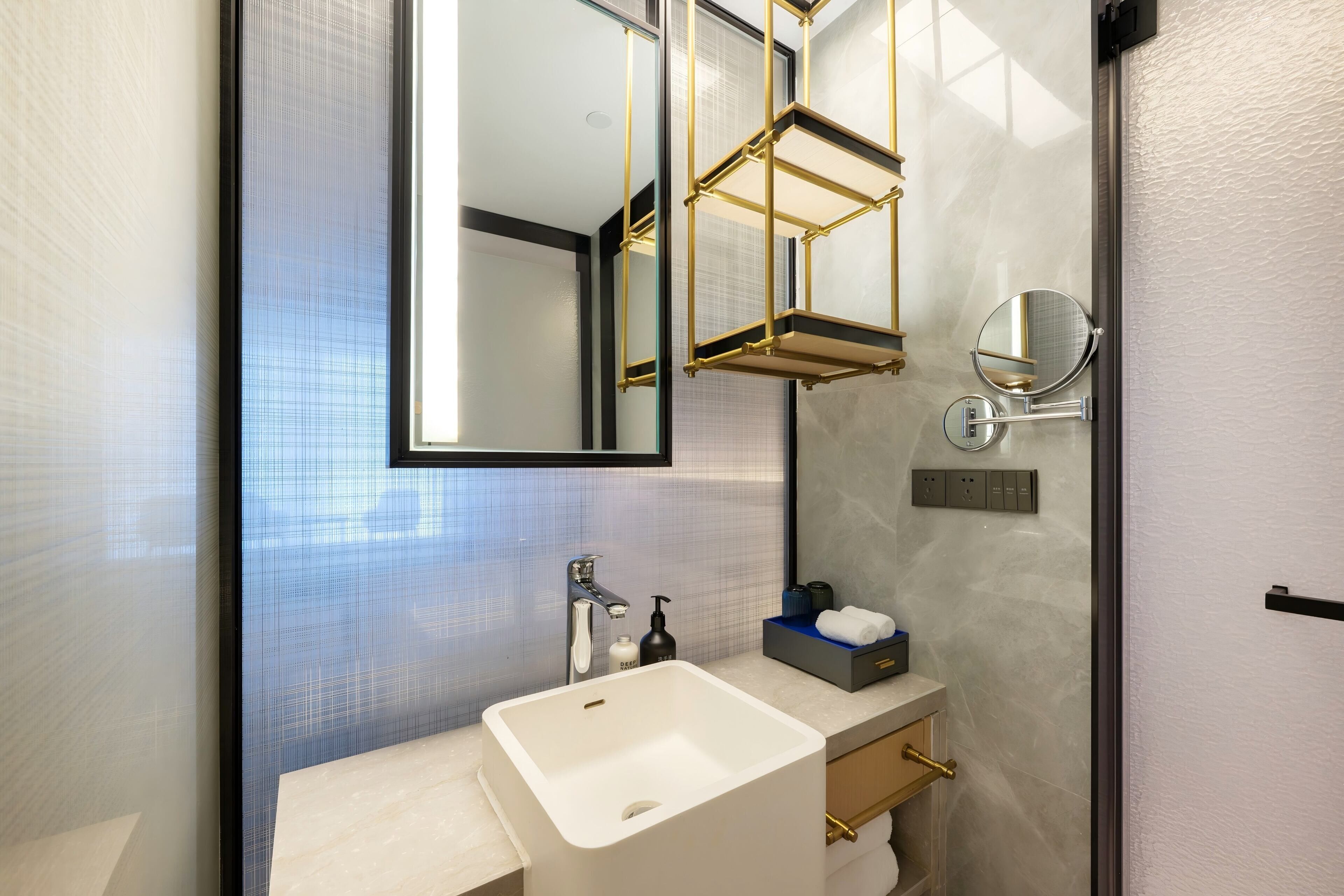 Une salle de bain moderne avec un grand miroir, un lavabo blanc, un porte-serviettes et une petite étagère contenant des articles de toilette.