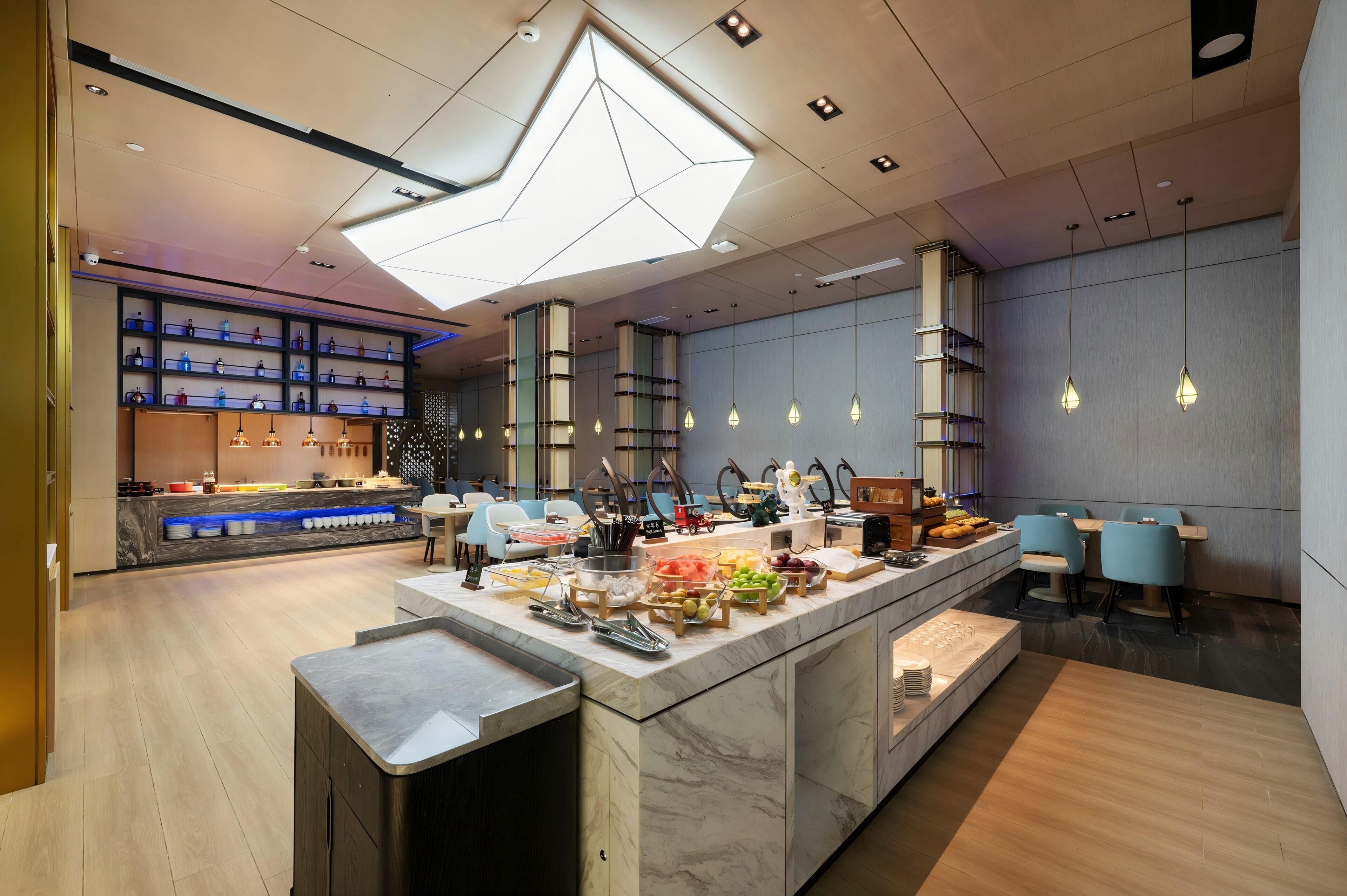 A modern kitchen with a central island, overhead lighting, and a seating area with blue chairs.