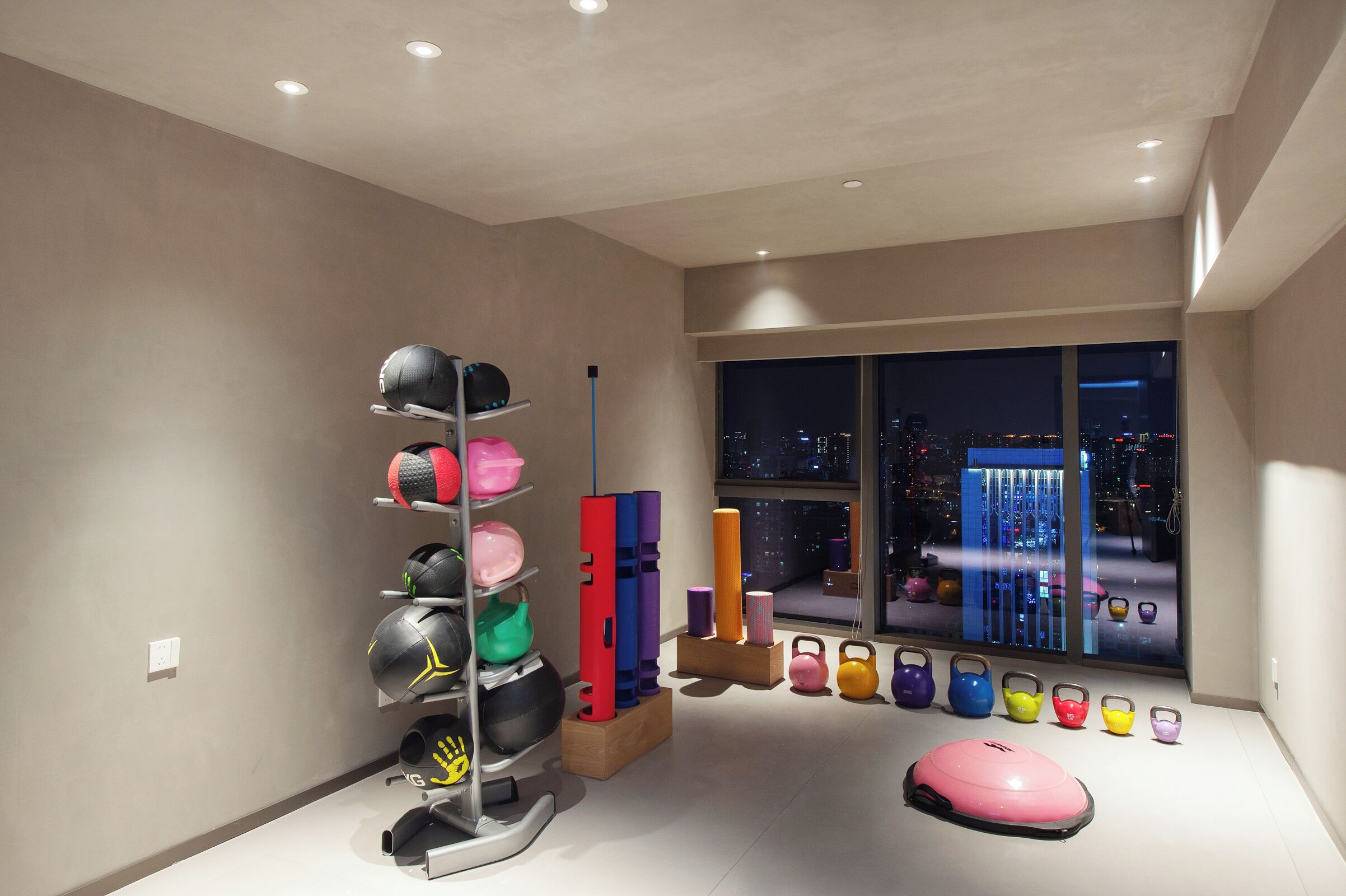 A room with a large window, a ceiling with recessed lighting, and a variety of exercise equipment.
