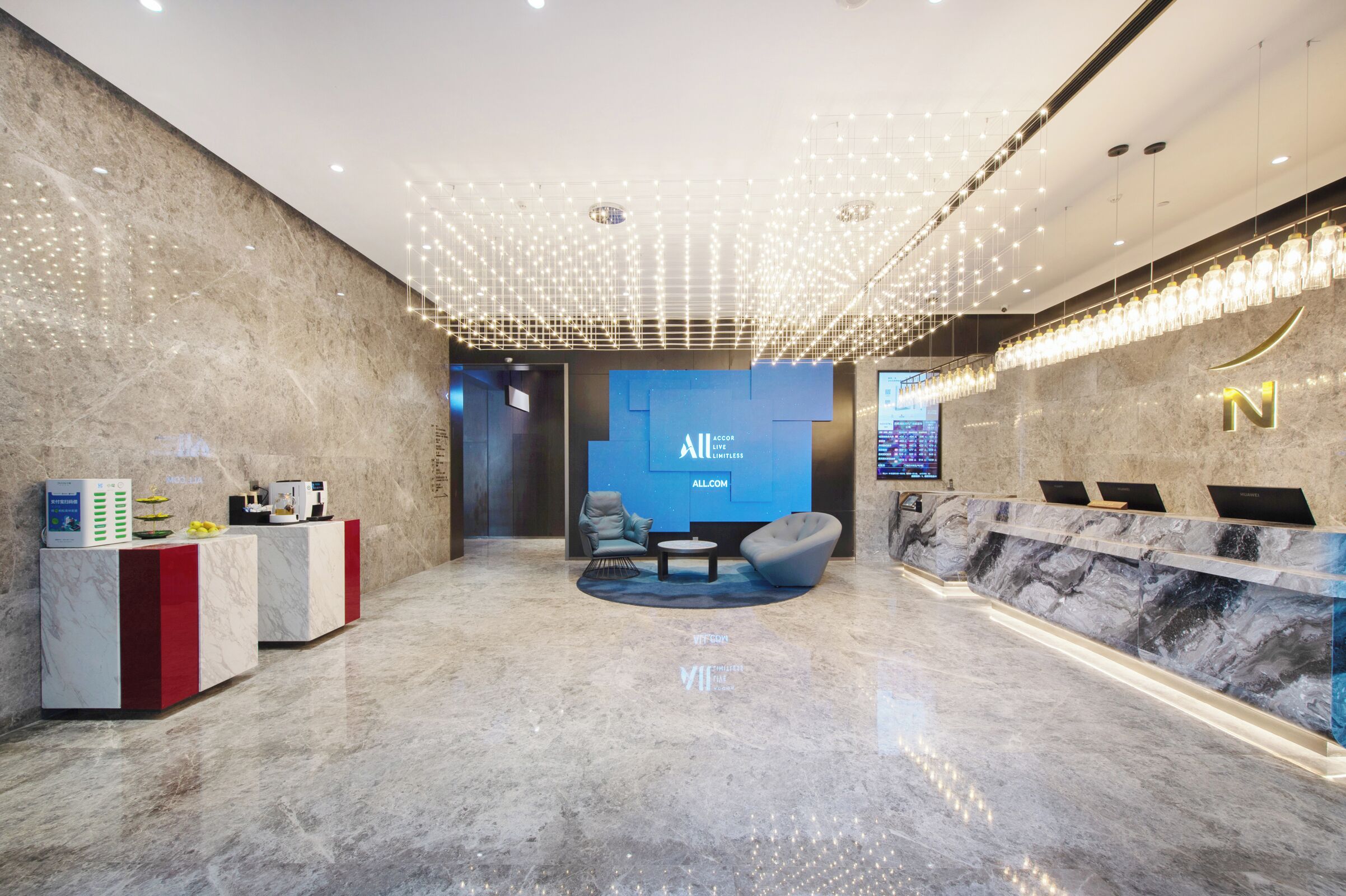 A modern reception area with a marble floor, a blue wall with 'AllCom' branding, a seating area with a round table, and a reception desk with a 'N' logo.