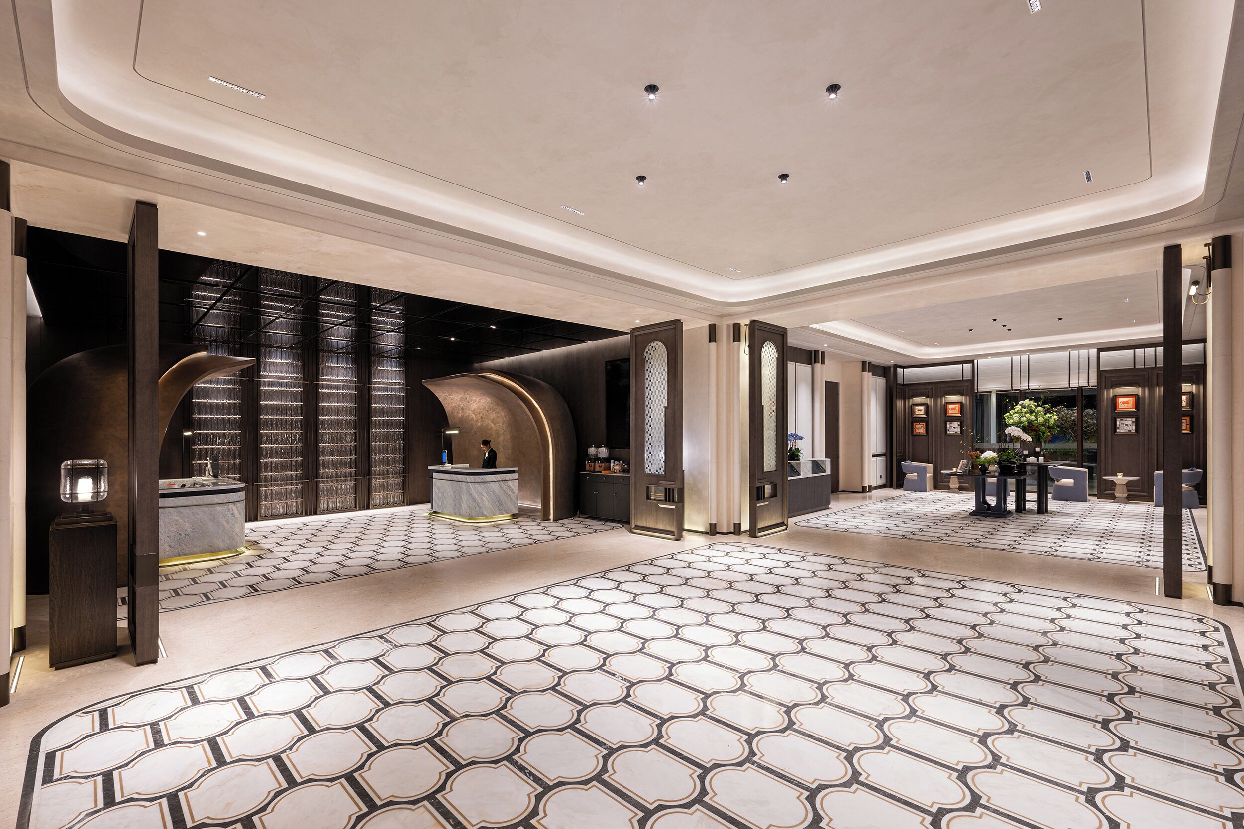 Een ruime lobby met een vloer met geometrisch patroon, moderne verlichting en een receptie met balie en zitplaatsen.