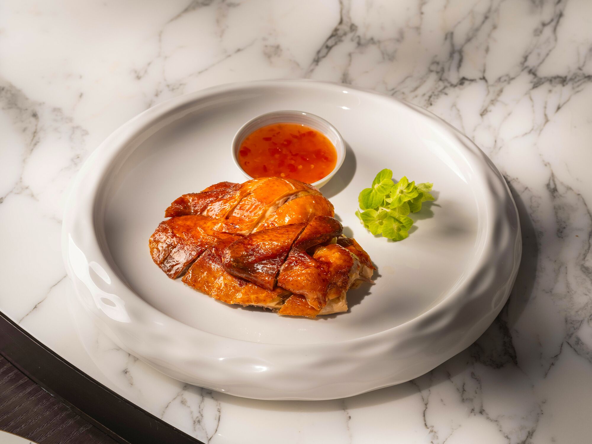 Un plato con un guiso de pollo, un recipiente pequeño con salsa y una guarnición de hojas verdes.