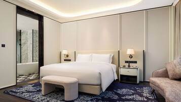 A modern hotel room with a large bed, bedside tables, a bench, and a patterned rug.