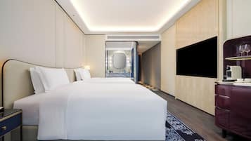 A hotel room with a large bed, a TV, a desk with a coffee maker, and a bathroom visible in the background.