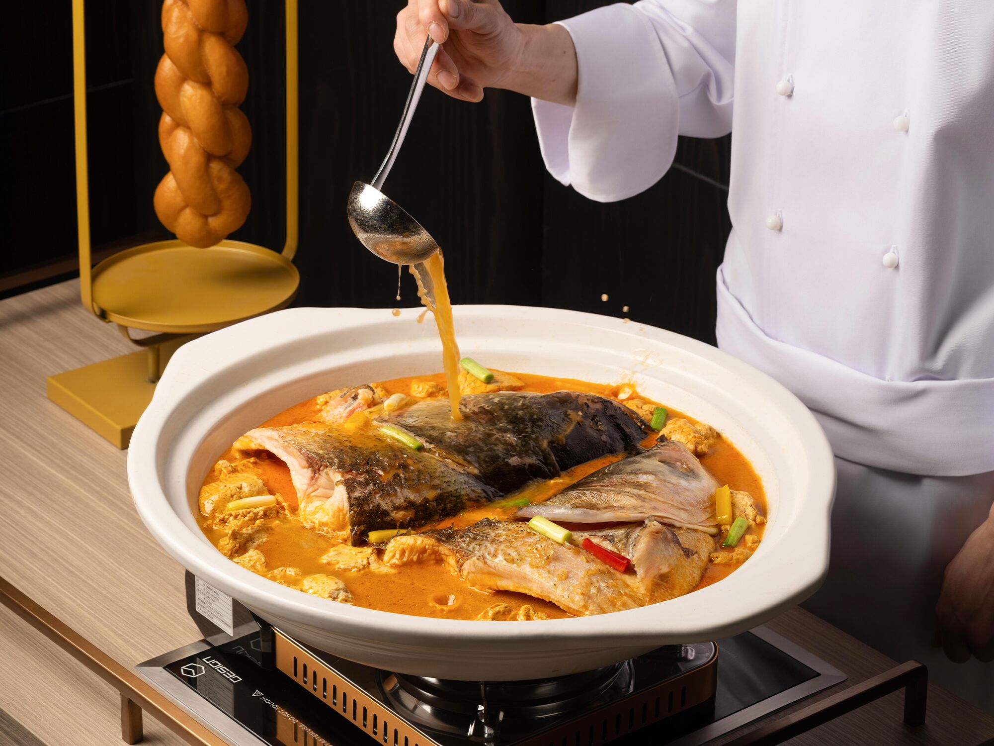 Un chef vertiendo salsa sobre un pescado en un bol blanco sobre una estufa.