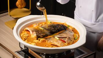 Un chef vertiendo salsa sobre un pescado en un bol blanco sobre una estufa.