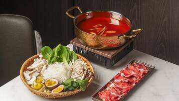 Una preparación de olla caliente con un caldo rojo, una bandeja de carne cruda y una cesta de verduras y hongos.