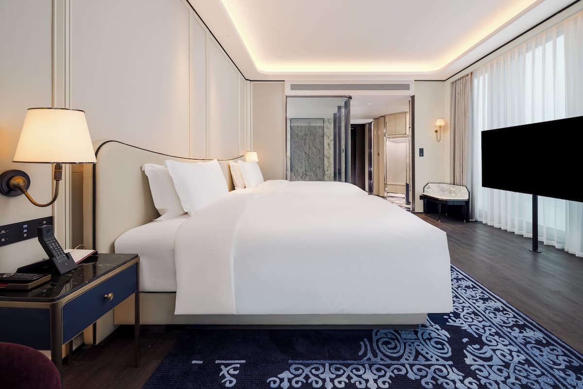 A modern hotel room with a large bed, bedside lamps, a desk with a telephone, and a television.