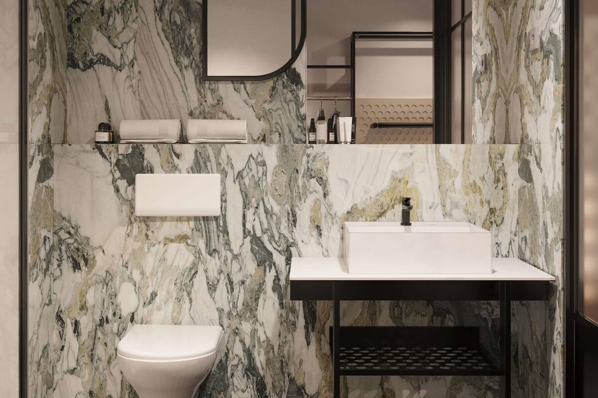 A bathroom with a marble wall, a toilet, a sink, and a mirror.