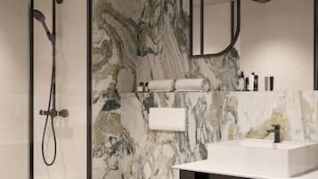 A modern bathroom with a glass shower enclosure, a toilet, a sink with a black countertop, and a marble backsplash.