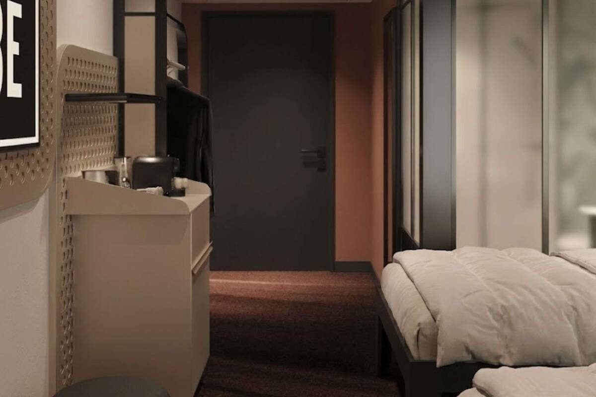 A hotel room with a bed, a desk, and a chair. There is a door leading to another room.