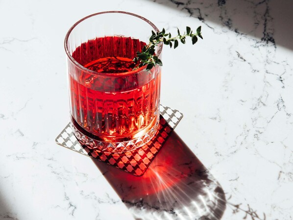 A glass of red beverage on a marble surface with a geometric coaster.