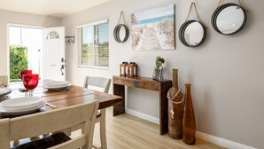 A dining area with a wooden table, chairs, and a bench. There are two hanging mirrors on the wall and a painting above the bench. - Walk To Ponto Beach - Surf and Relax (Carlsbad)