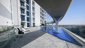 Ein Poolbereich auf dem Dach mit Liegestühlen, ein modernes Gebäude im Hintergrund und ein klarer Himmel.