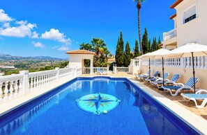 A swimming pool with a compass design, surrounded by lounge chairs and umbrellas, with a view of the landscape and buildings in the background. - Villa Atria - stunning Moraira views (Moraira)
