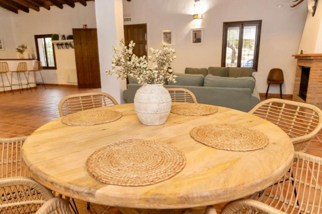 A round wooden table with woven placemats, surrounded by wicker chairs, in a room with a green sofa and a fireplace.