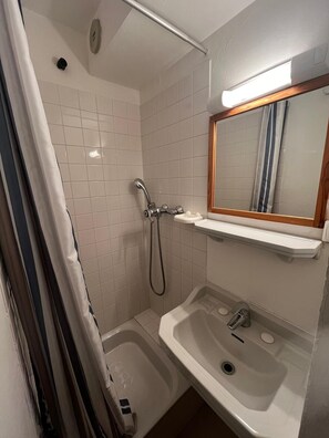 A small bathroom with a shower, a sink, and a mirror.