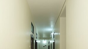 Ein langer, schmaler Korridor mit Türen an beiden Seiten, einem Mülleimer und einer Deckenleuchte.