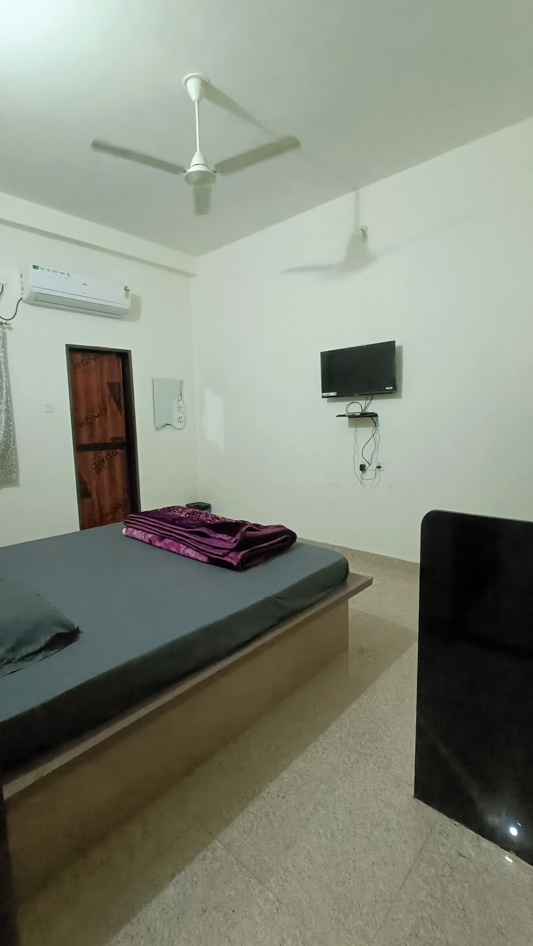 Ein Schlafzimmer mit einem Bett, einem Deckenventilator, einer Klimaanlage, einem Fernseher und einer Tür.