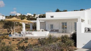 Una villa moderna y blanca con un área de estar exterior cubierta, vistas del paisaje circundante y un cielo azul despejado.