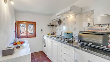 Une cuisine compacte avec des meubles blancs, un four encastré, un grille-pain et une fenêtre donnant sur des immeubles.